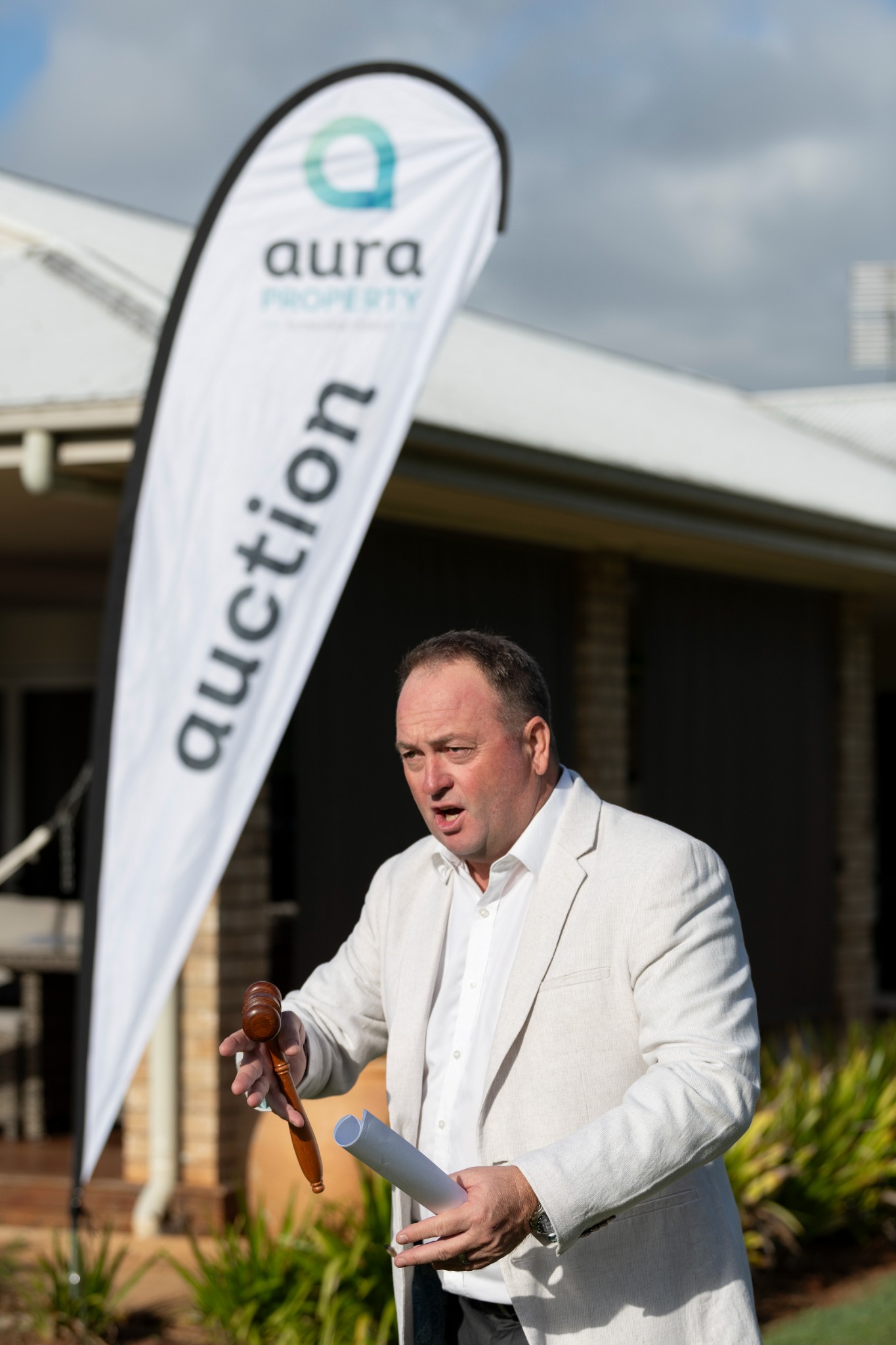 Darren Lockwood conducting an auction, holding a gavel beside an AURA auction flag